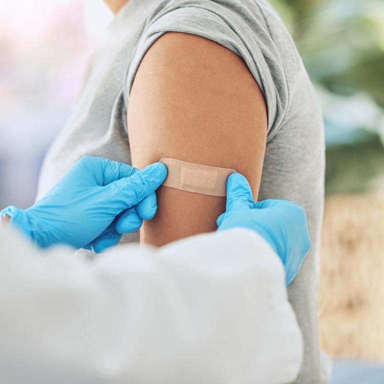 Doctor At An Onsite Flu Clinic Applying A Bandage To A Patients Arm