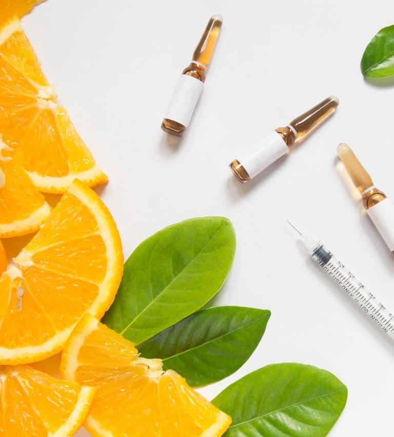 Orange Juice And Syringes For Vitamin Injections On A- White Surface